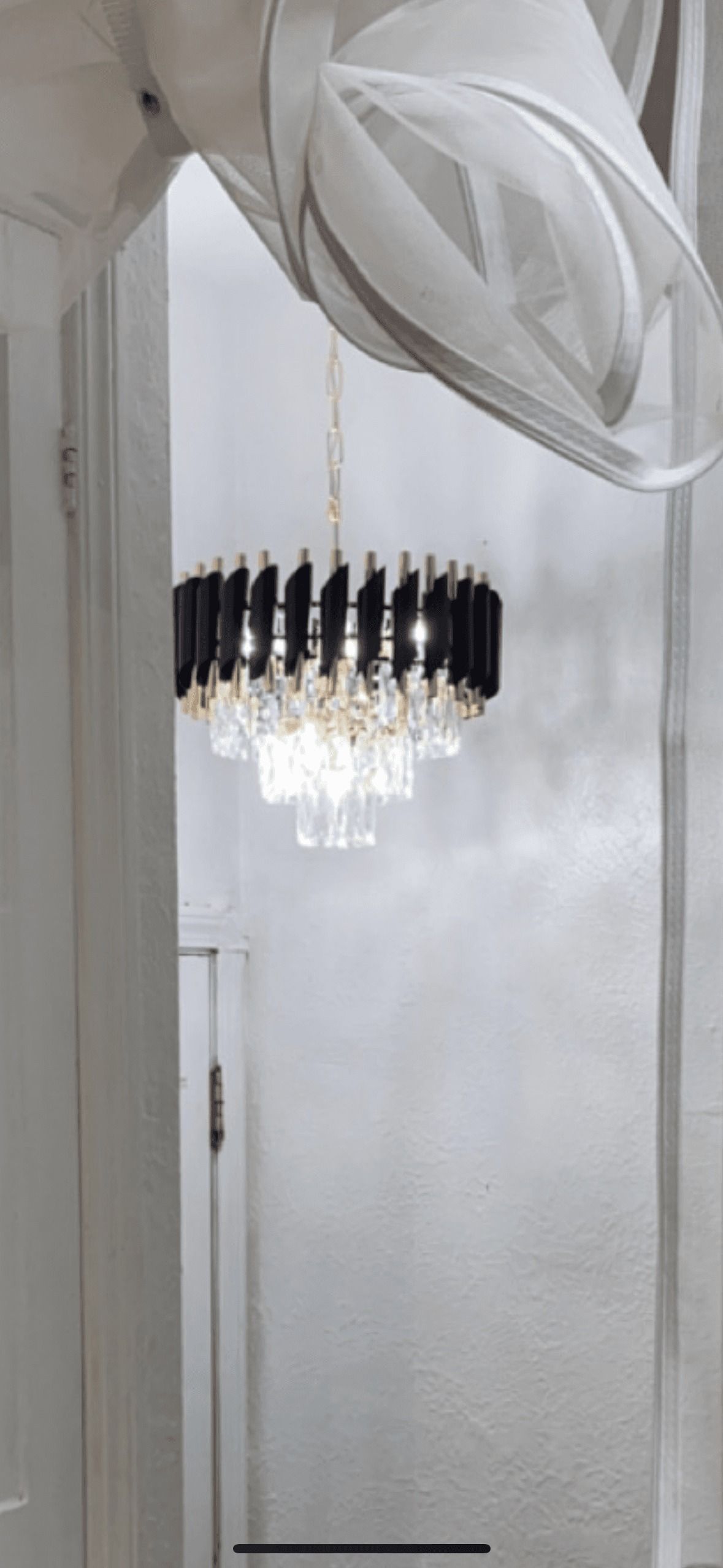 A decorative chandelier with black accents hangs in a white room.