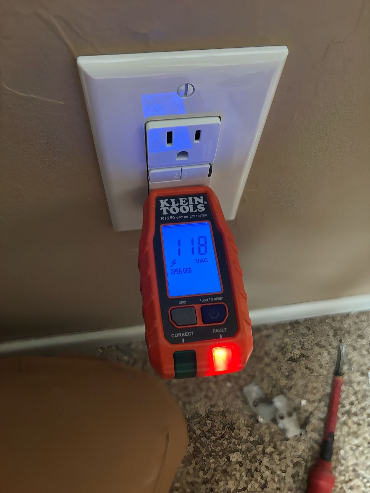 Electrical outlet tester showing 118 volts, with a lit red light, inserted into a wall outlet.