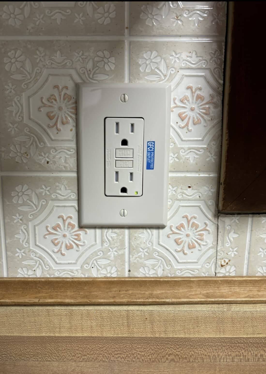 White GFCI outlet on patterned tile backsplash.
