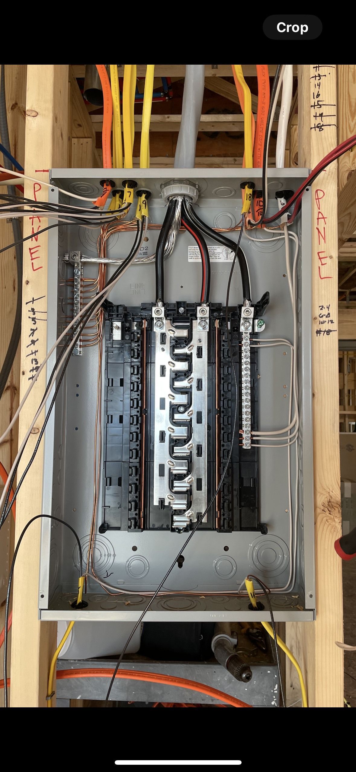 Electrical panel with wires connected. Inside a wooden frame, orange, yellow, and black wires.