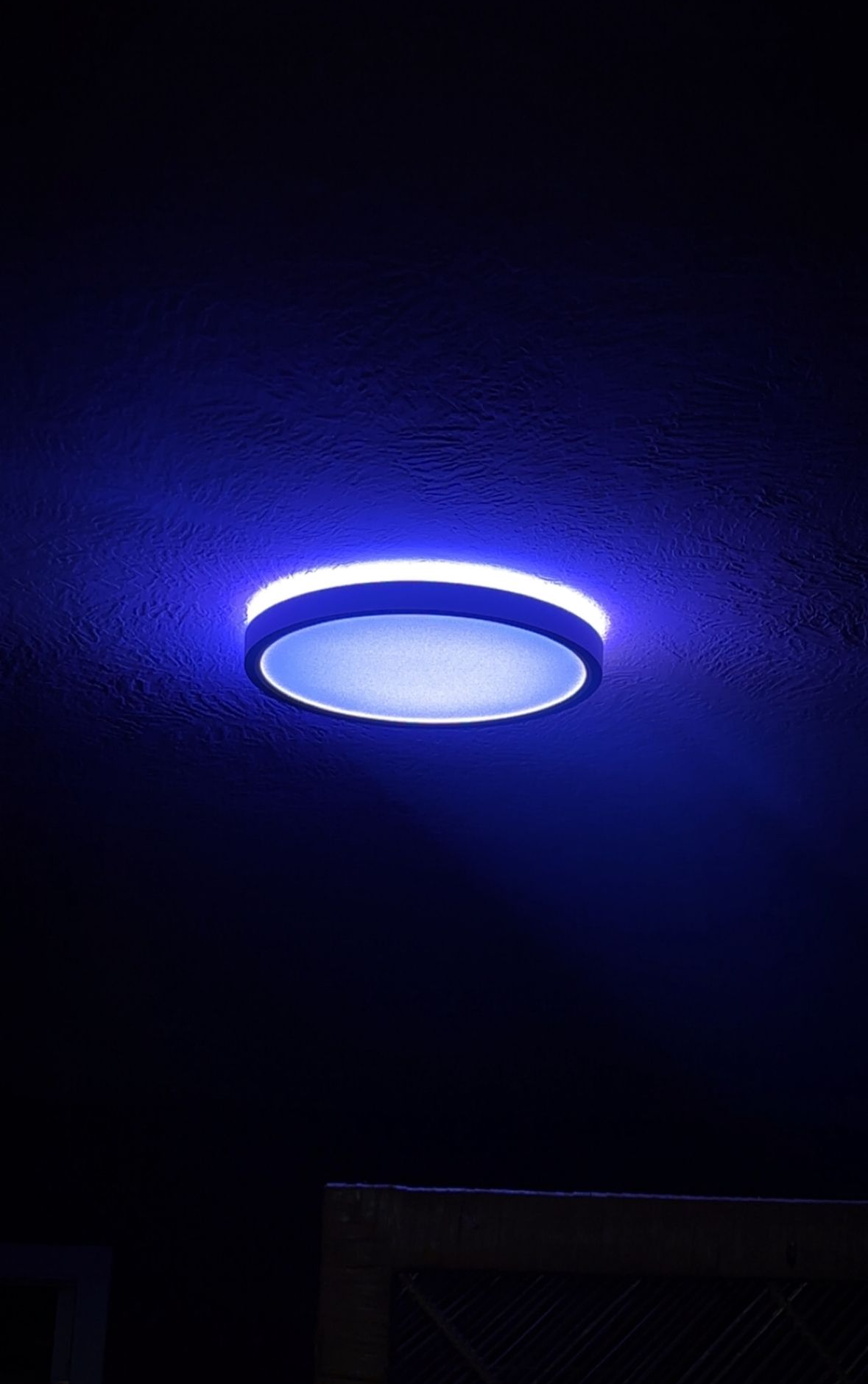 Blue, circular light fixture on a dark ceiling.