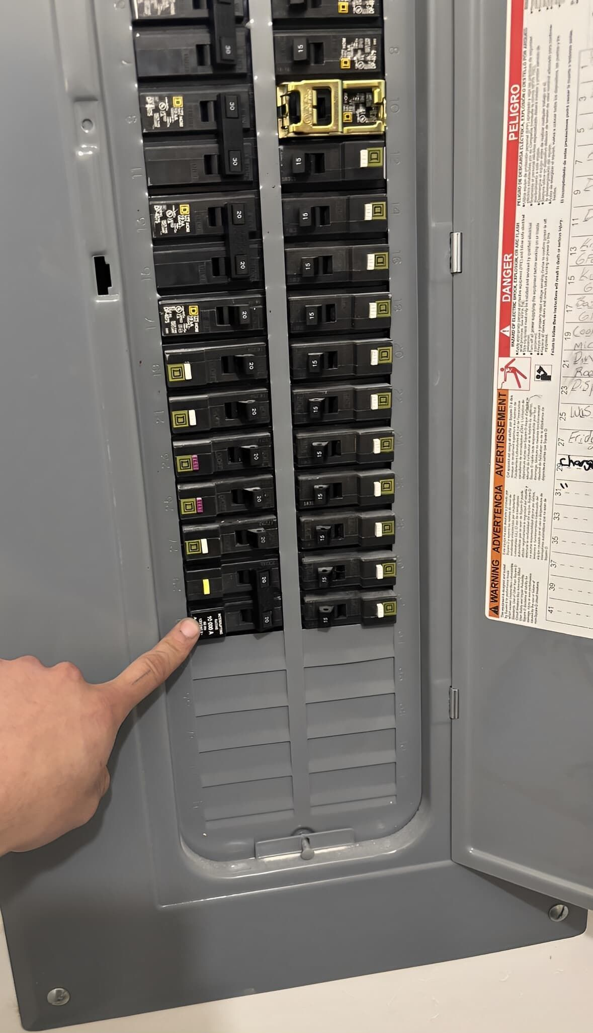 A hand points at a tripped circuit breaker in an open electrical panel.