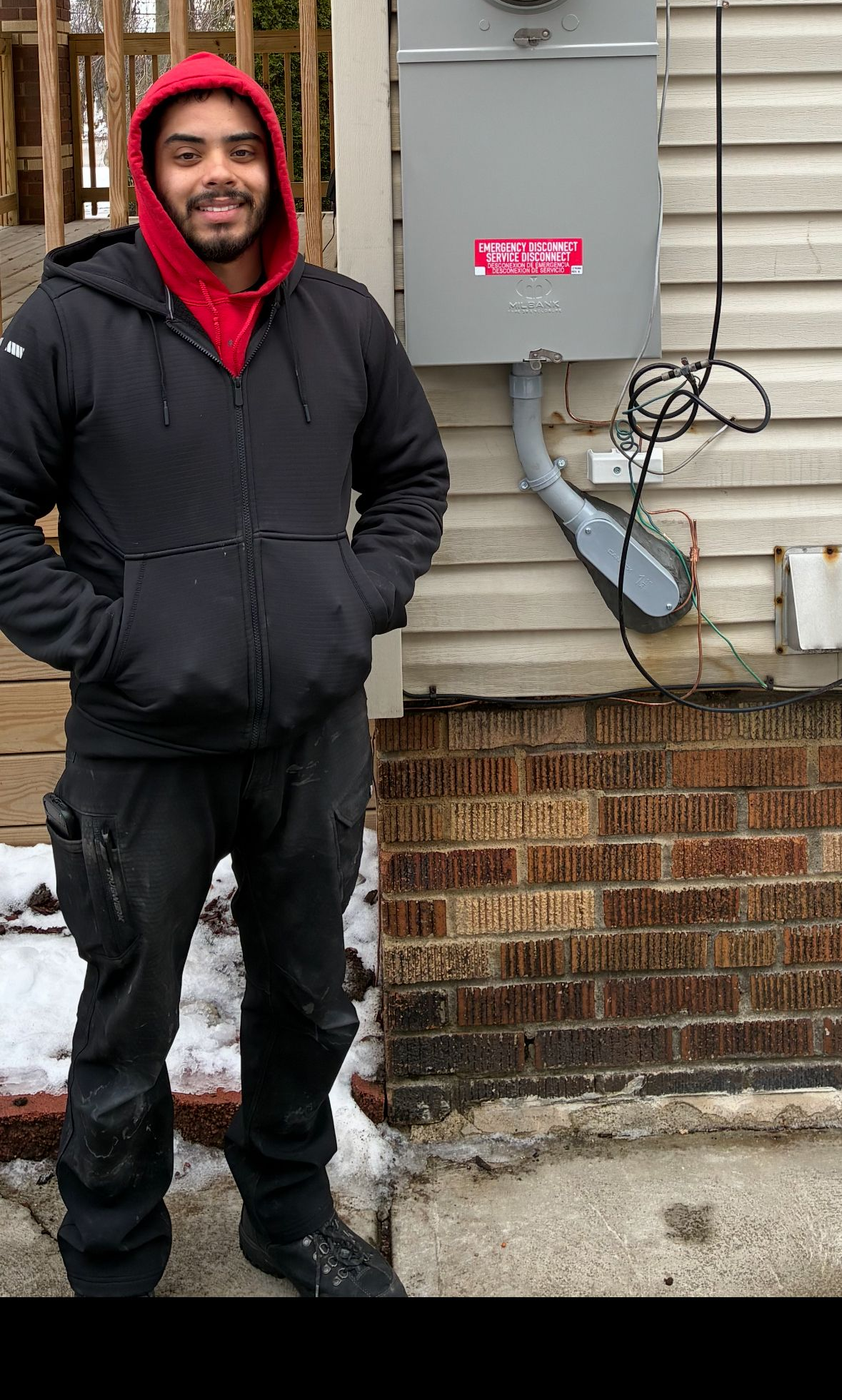 Electrical outlet box on a brick wall, with a multimeter plugged in. A finger points at the outlet.