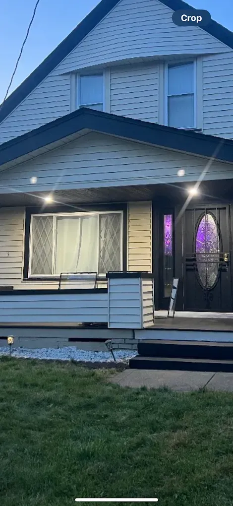 A two-story house with a black roof and door. A front porch with a window and a grassy lawn.