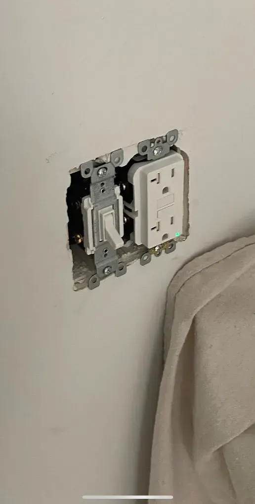 Electrical outlet and switch installed in a wall with exposed wiring and a gap around the devices.