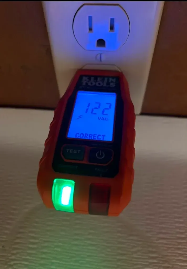 Orange electrical outlet tester plugged into a wall outlet, displaying 122V and 