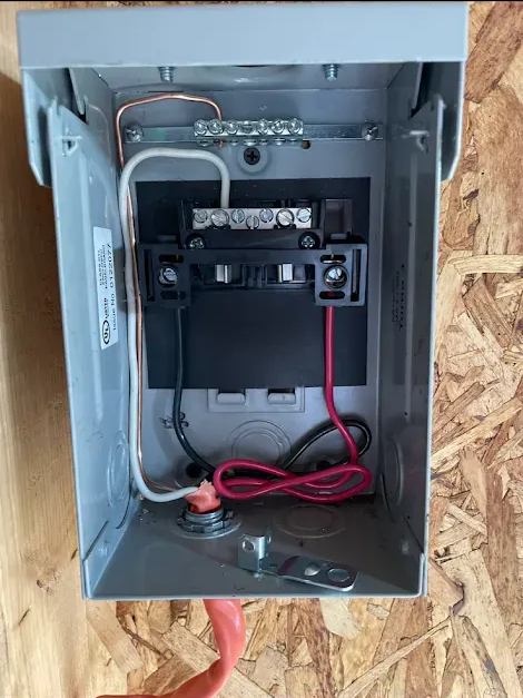 Open metal electrical junction box with wiring on wooden surface.