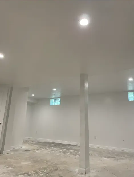 White-walled basement with concrete floor, recessed lights, and support beams.