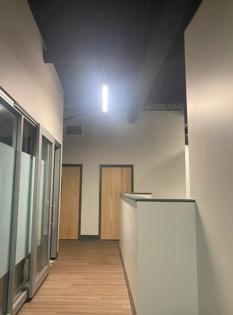 Hallway with glass-walled offices on the left, two wooden doors, and a white counter with a light fixture on the ceiling.