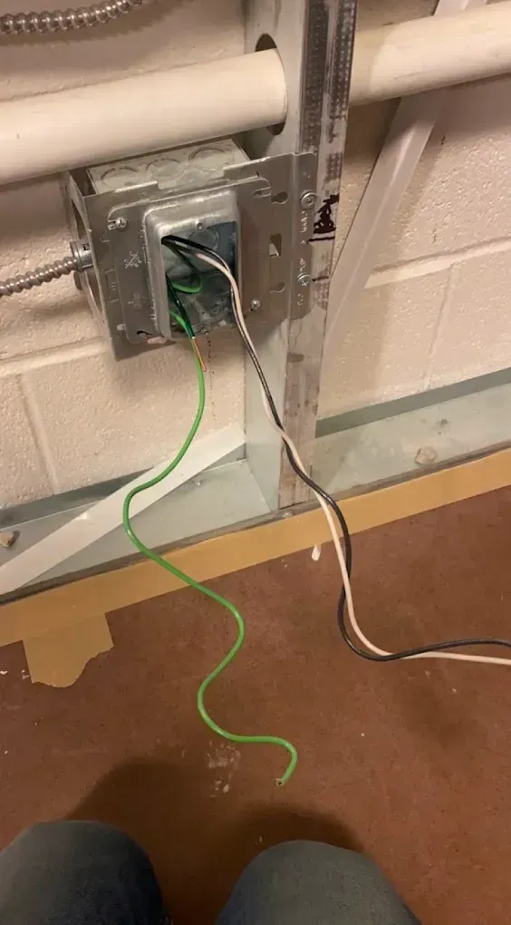 Electrical junction box with exposed wires: green, black, and white. Located on a wall, with conduit above.