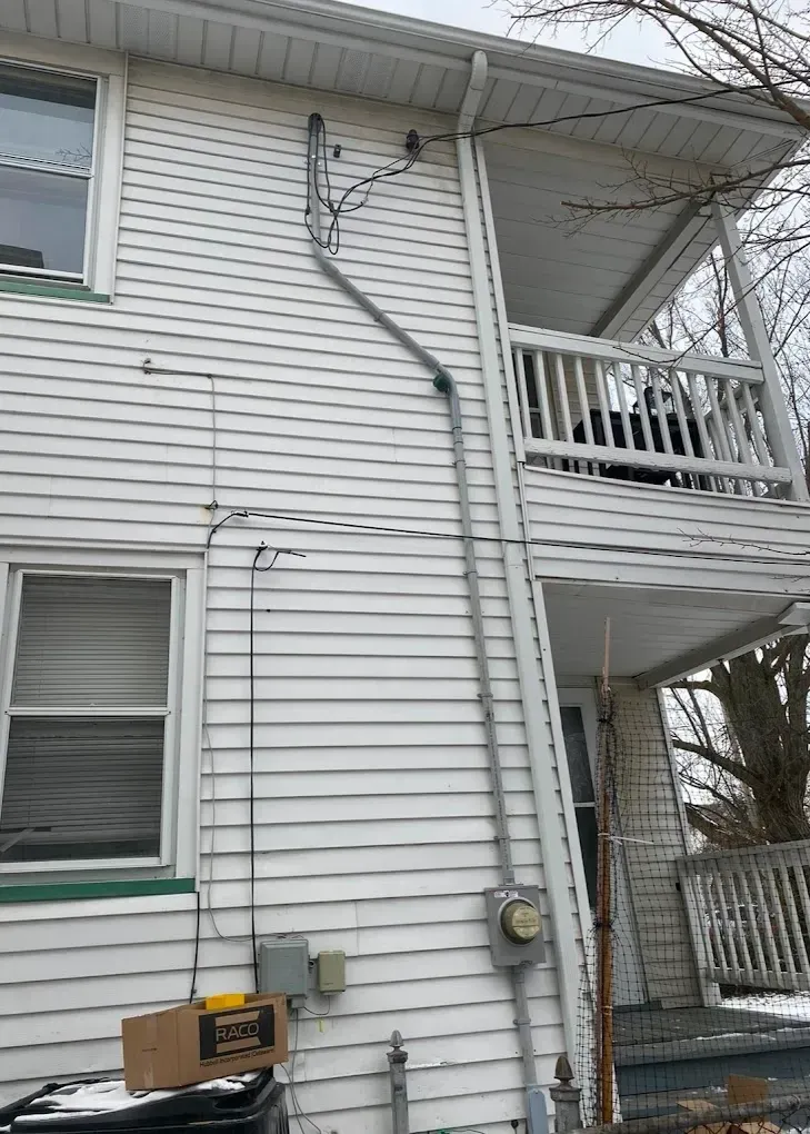 Exterior of a two-story white house with electrical wiring and a porch on the right side.