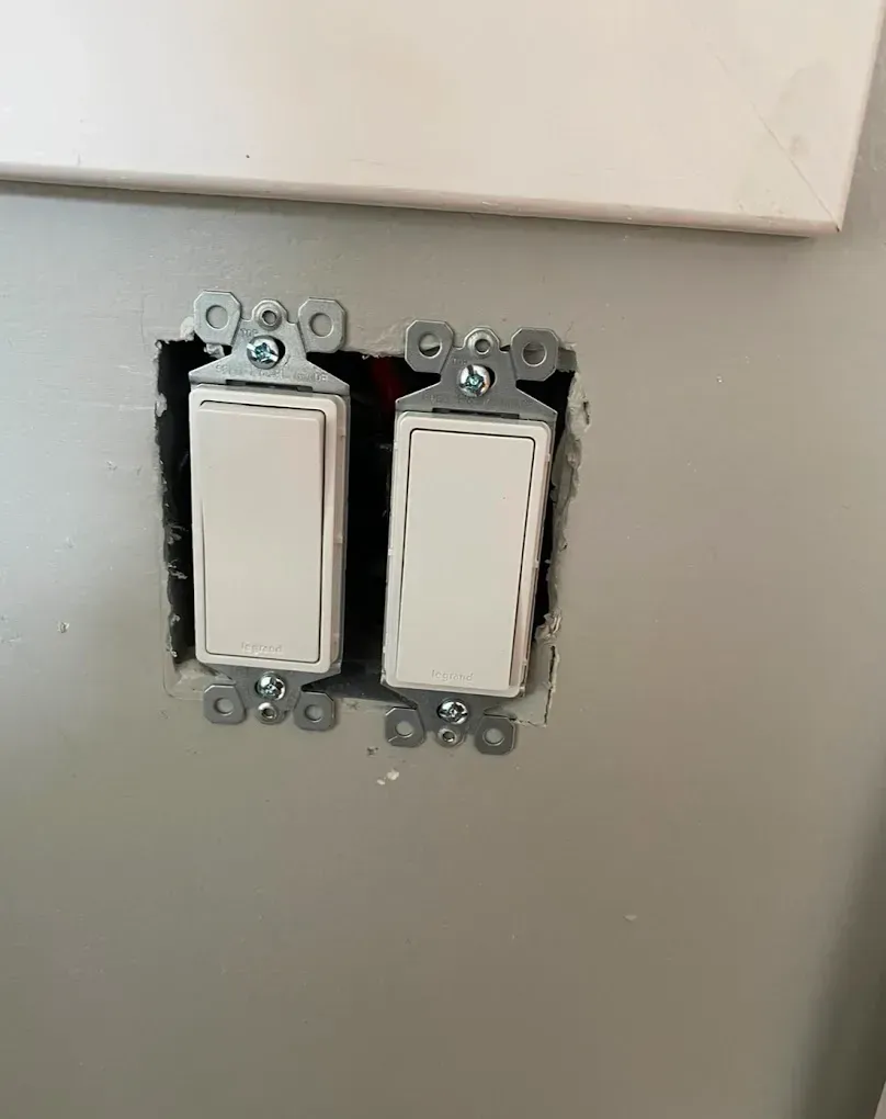 Two white light switches in a gray wall. The switches are partially installed in an electrical box.