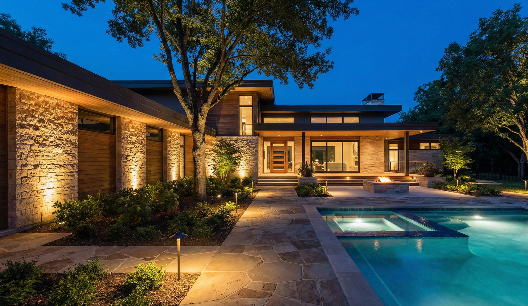 Lush green lawn with a tree lit by ground and pathway lights at dusk.