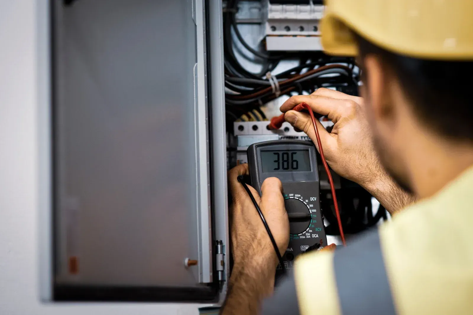 Electrician using a multimeter to test wiring inside an electrical panel.