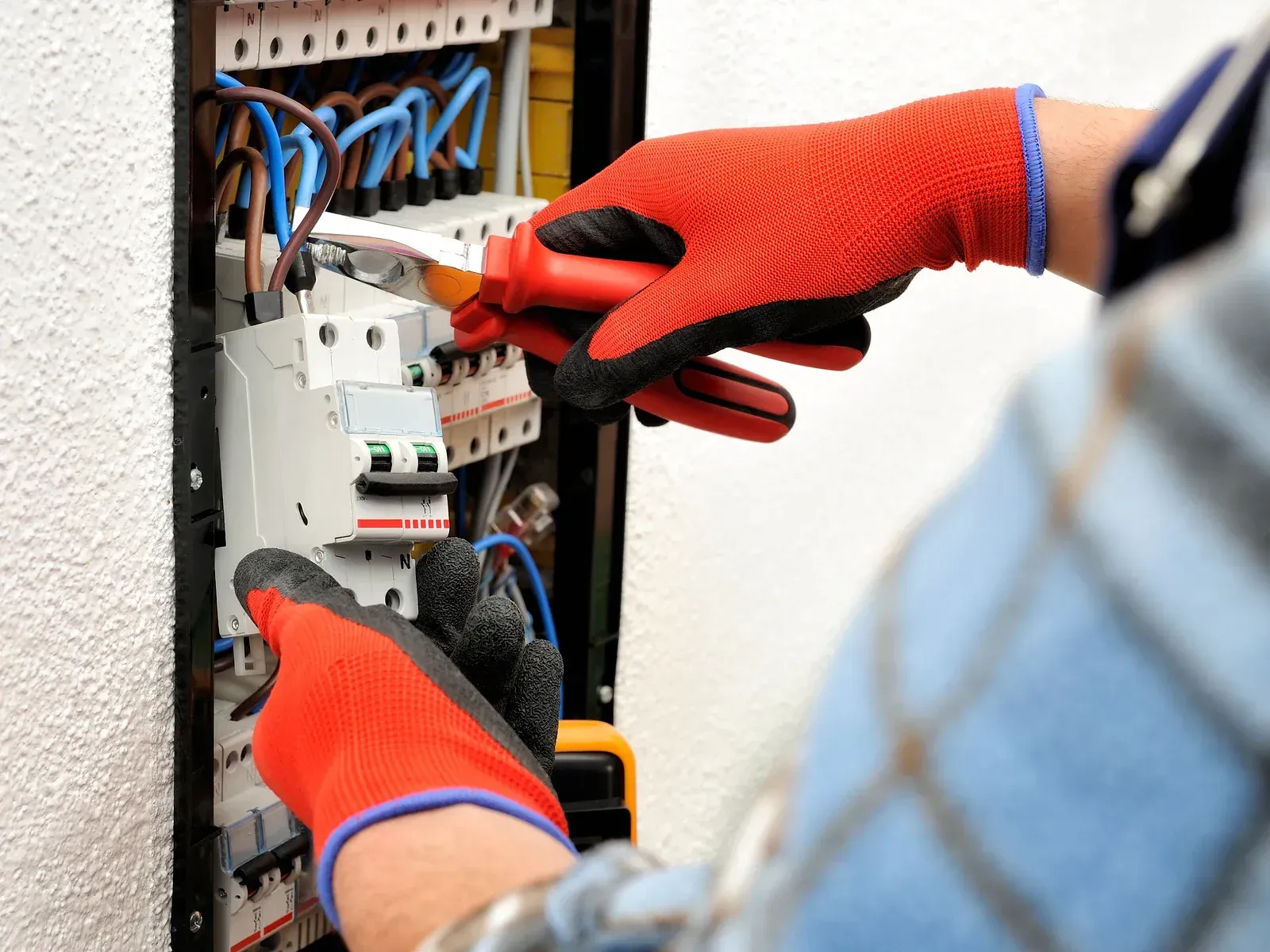 Electrician in red gloves working on an electrical panel, using a screwdriver.