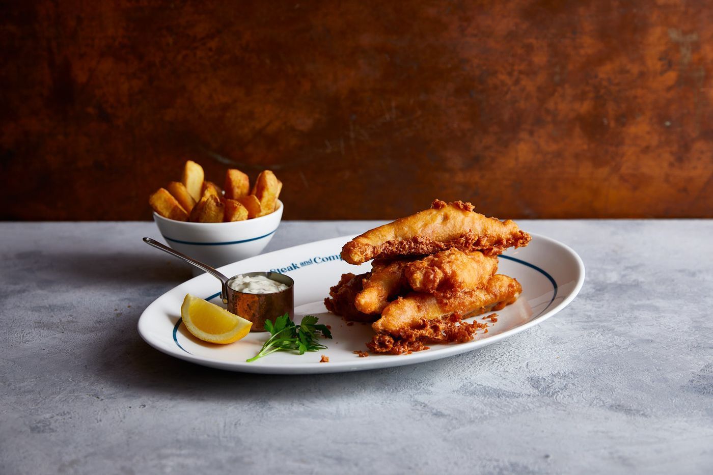 Plate of breaded chicken, arugula salad, and drink on marble table.