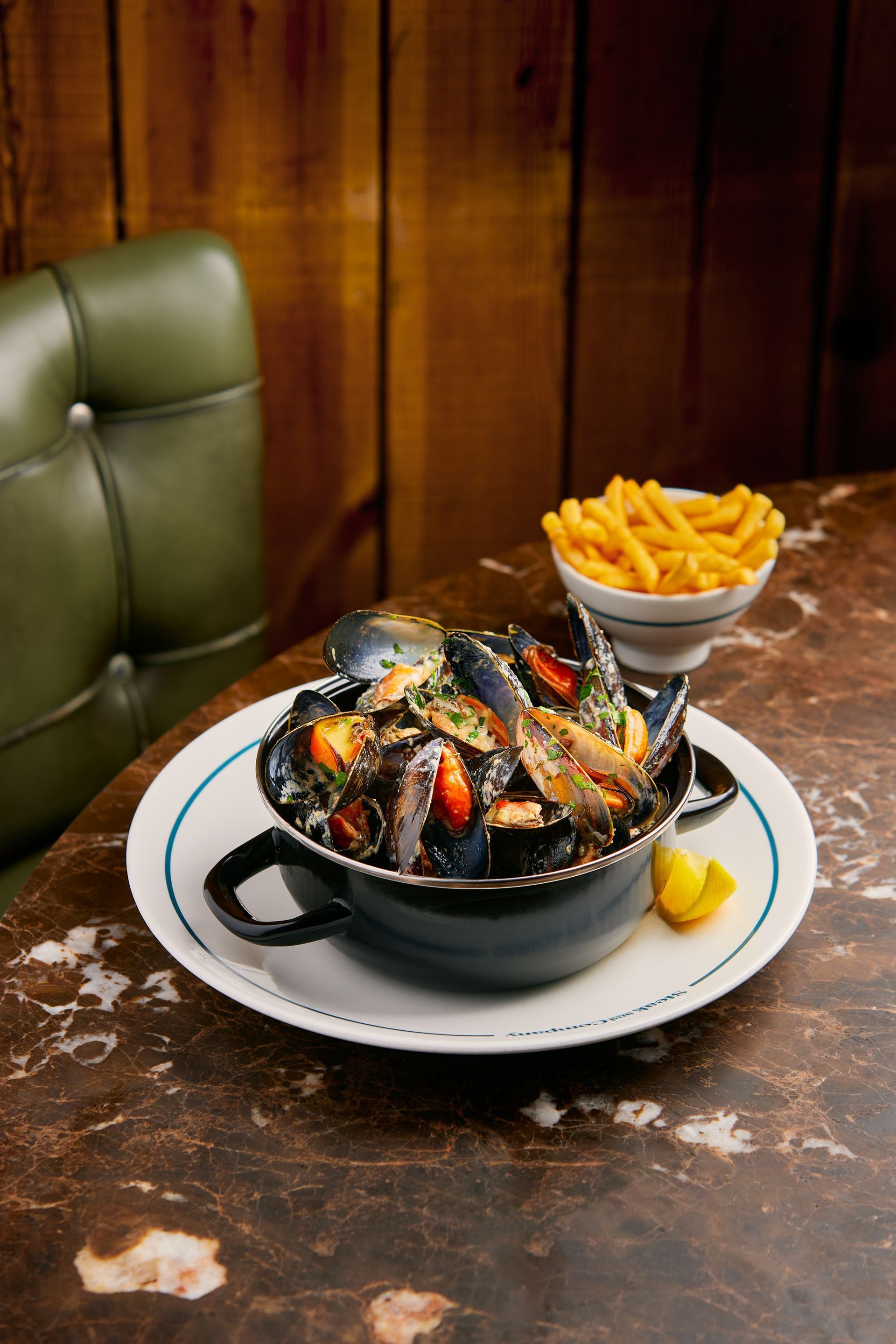 Mussels with fries on marble table in restaurant setting; green chair in background.