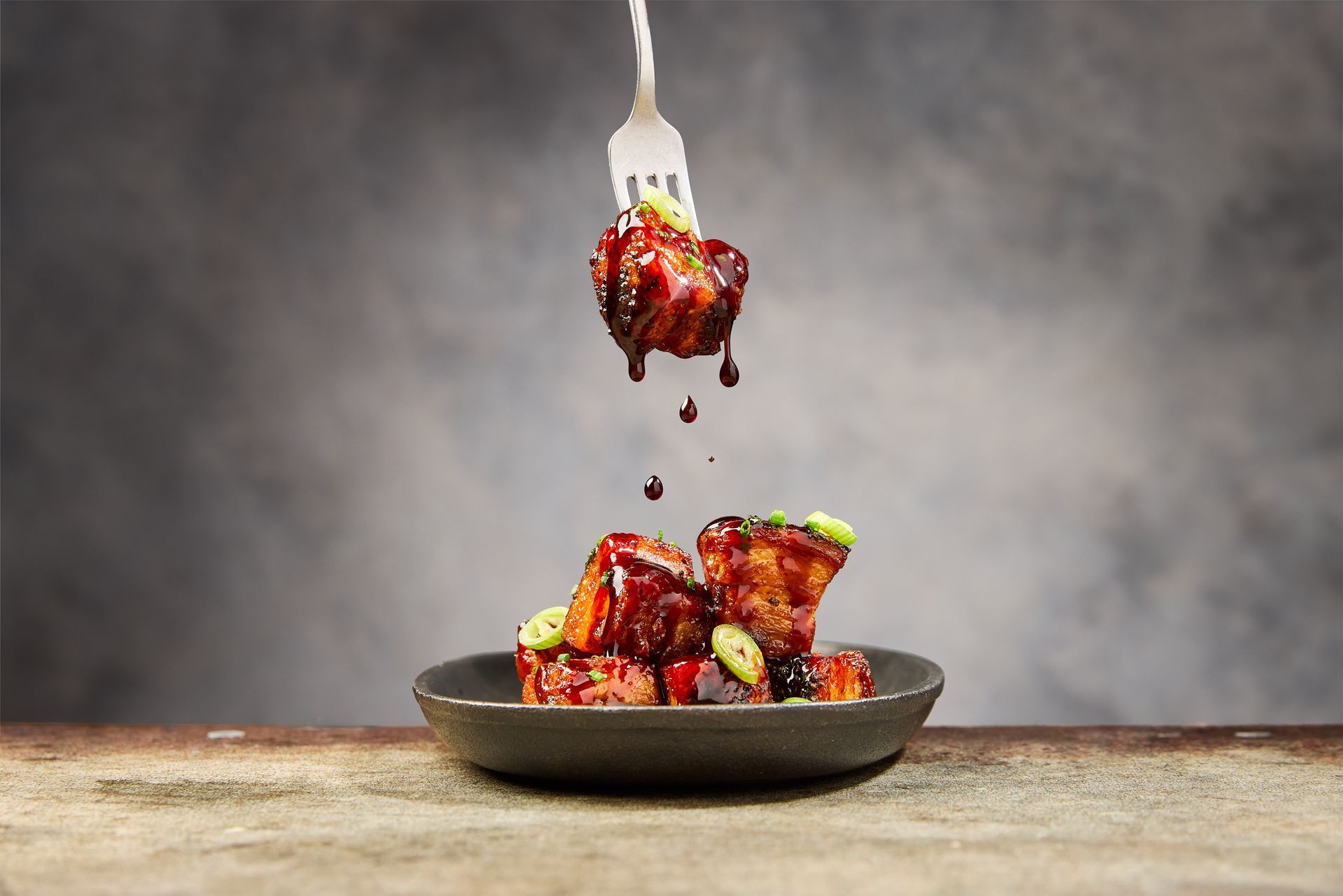 Fork lifting glazed pork cubes from a plate, sauce dripping.