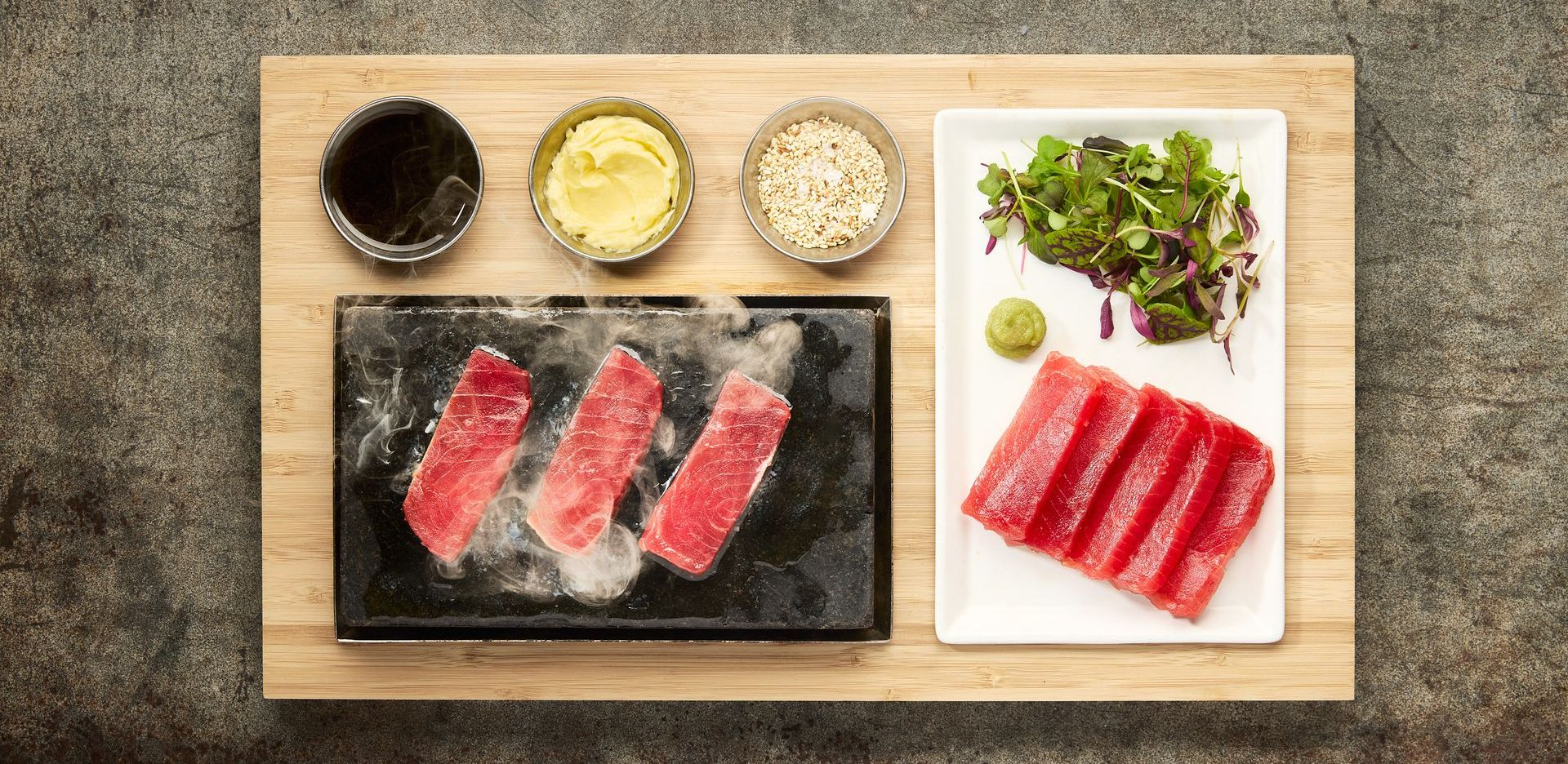 Sushi dish with tuna slices, sauces, and greens on a wooden board.