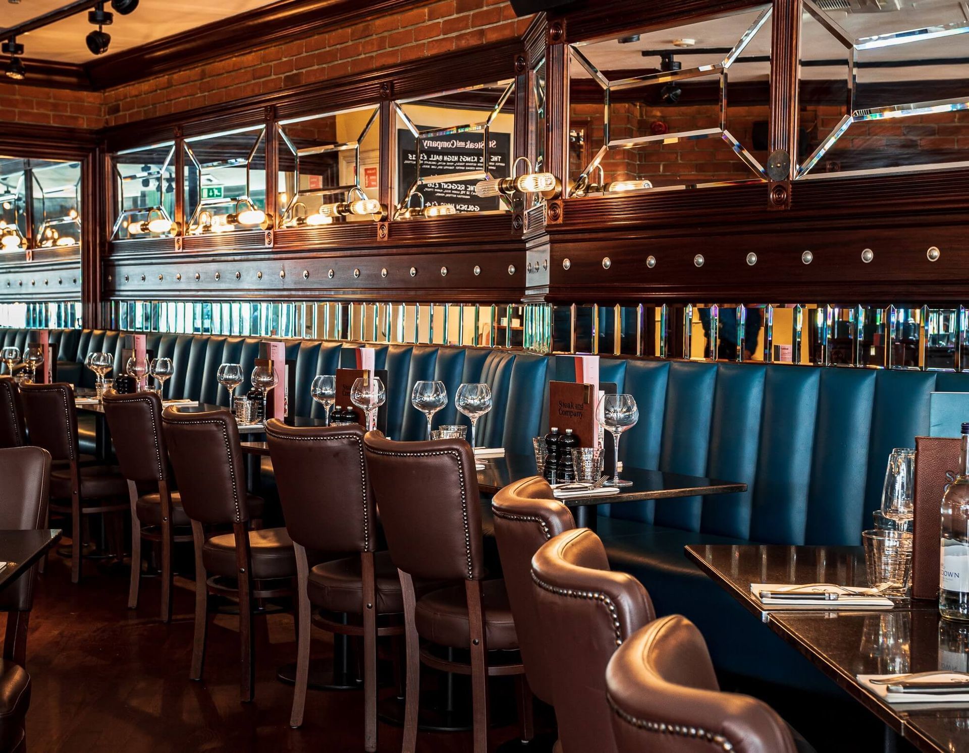 Restaurant interior with dark tables and chairs, large windows, and wood paneling.