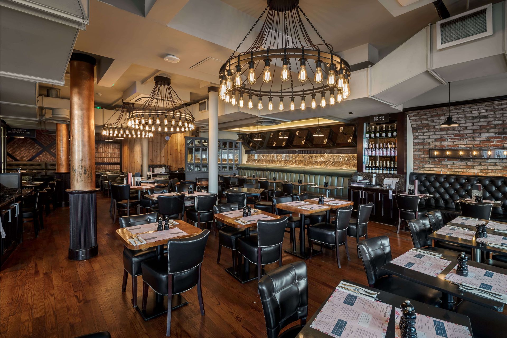 Restaurant interior with diners at tables, server stands at center. Exposed brick, industrial ceiling.