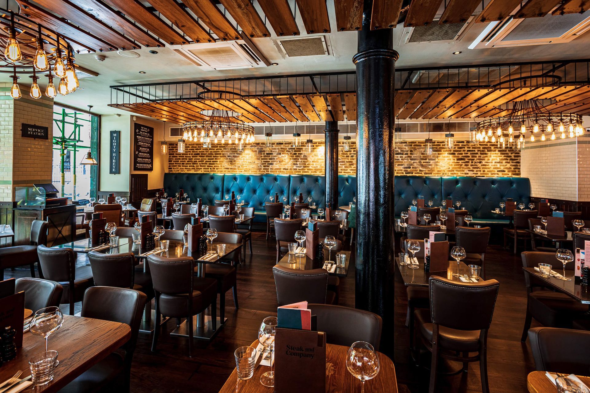Restaurant interior with tables, chairs, and overhead lighting; a central black pillar.