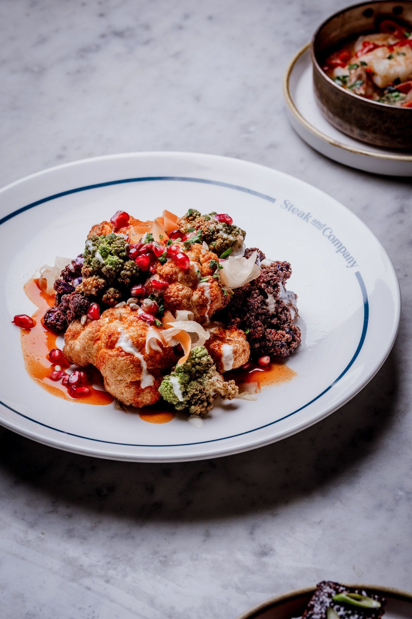 Cauliflower and broccoli dish on a plate with sauce, sprinkled pomegranate seeds.