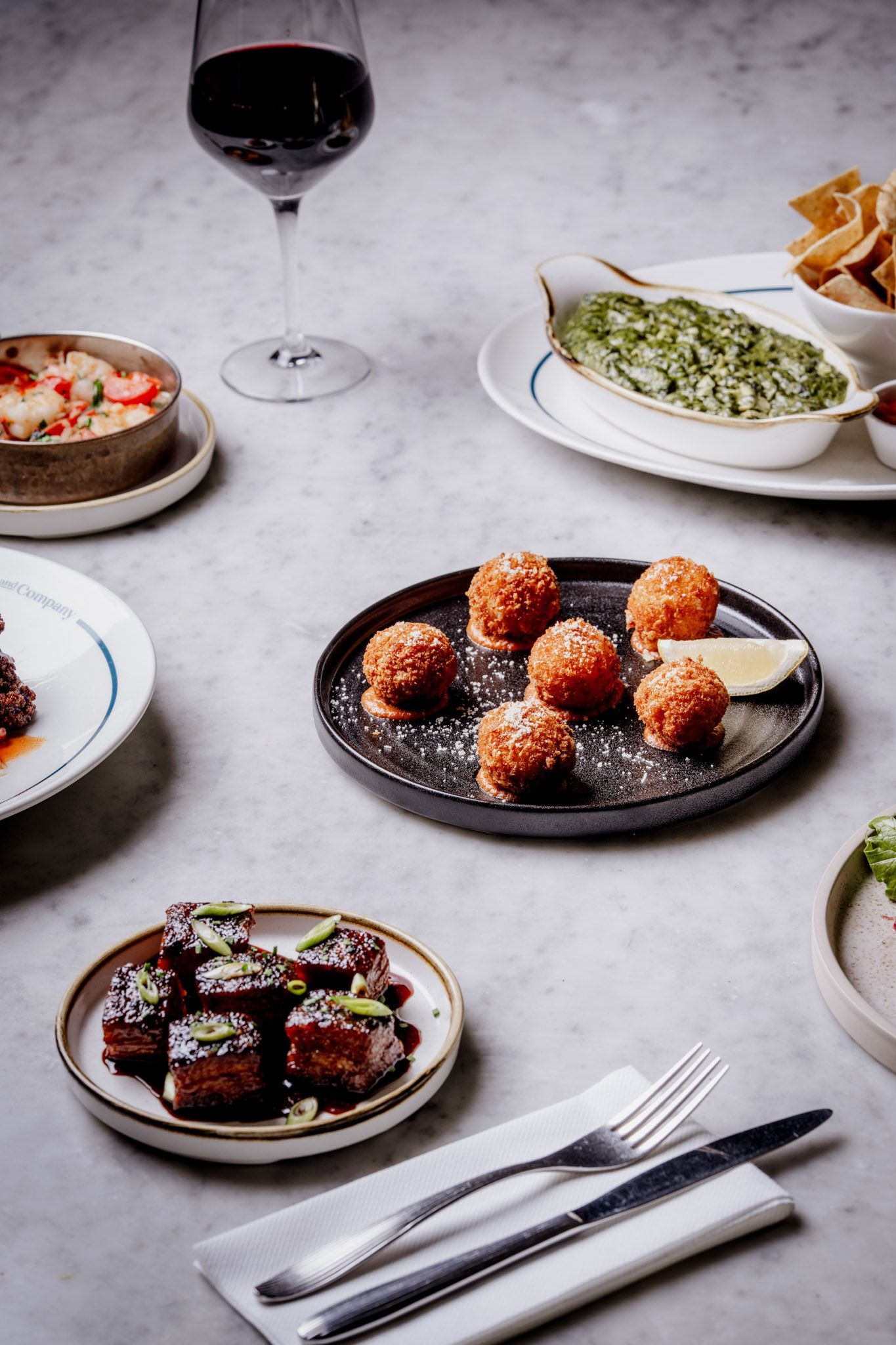 Various appetizers with a glass of red wine on a marble table.