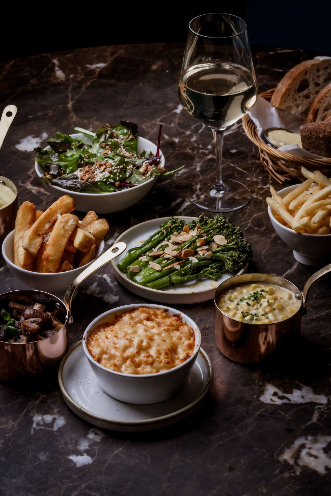 Table of various dishes: salad, fries, mac and cheese, asparagus, bread, butter, and wine.