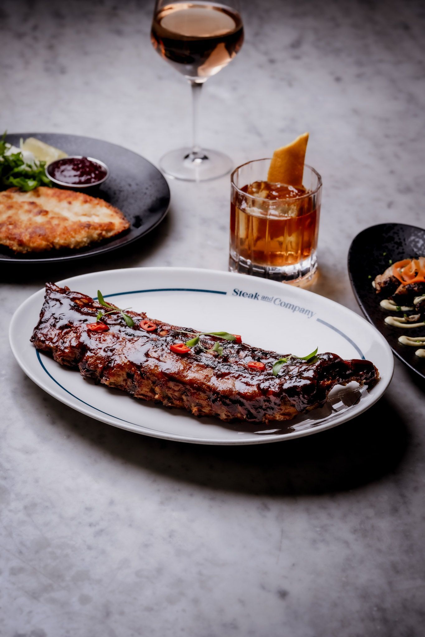 Plated ribs, cocktails, and other dishes on a marble surface.