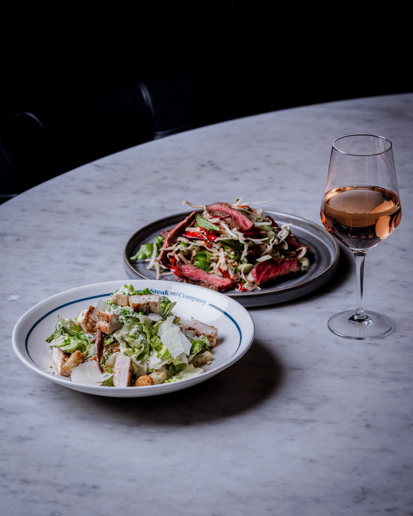 Two salads and a glass of rose wine on a marble table.