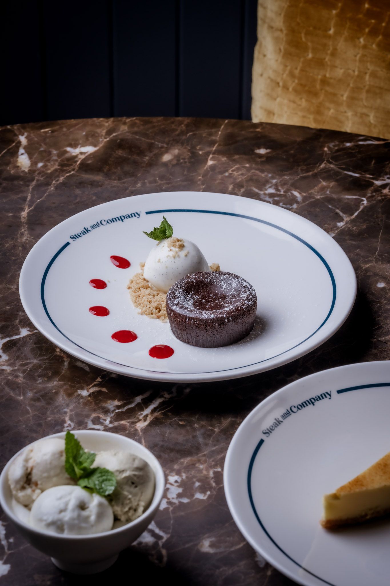 Chocolate lava cake with ice cream, berries, and a side of cheesecake on marble tabletop.
