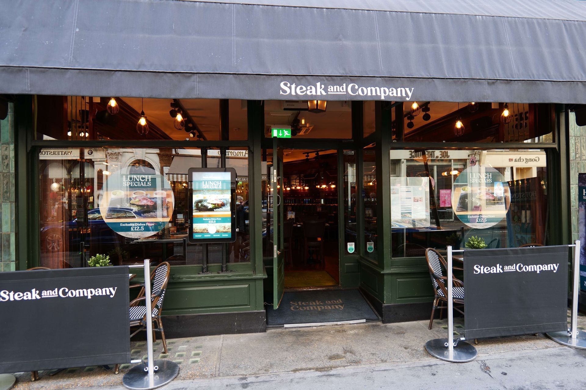 Restaurant interior with leather chairs and booths, tables set with glassware, and mirrored wall.