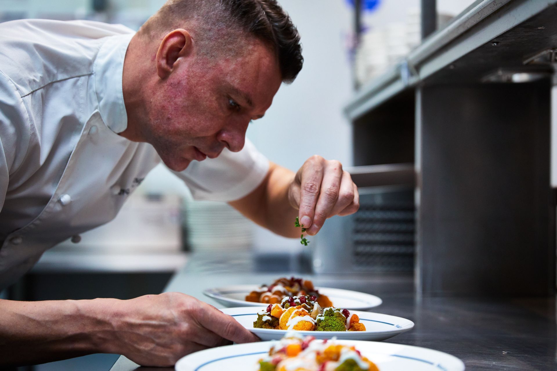 Chef carefully garnishing plates of food in a professional kitchen.
