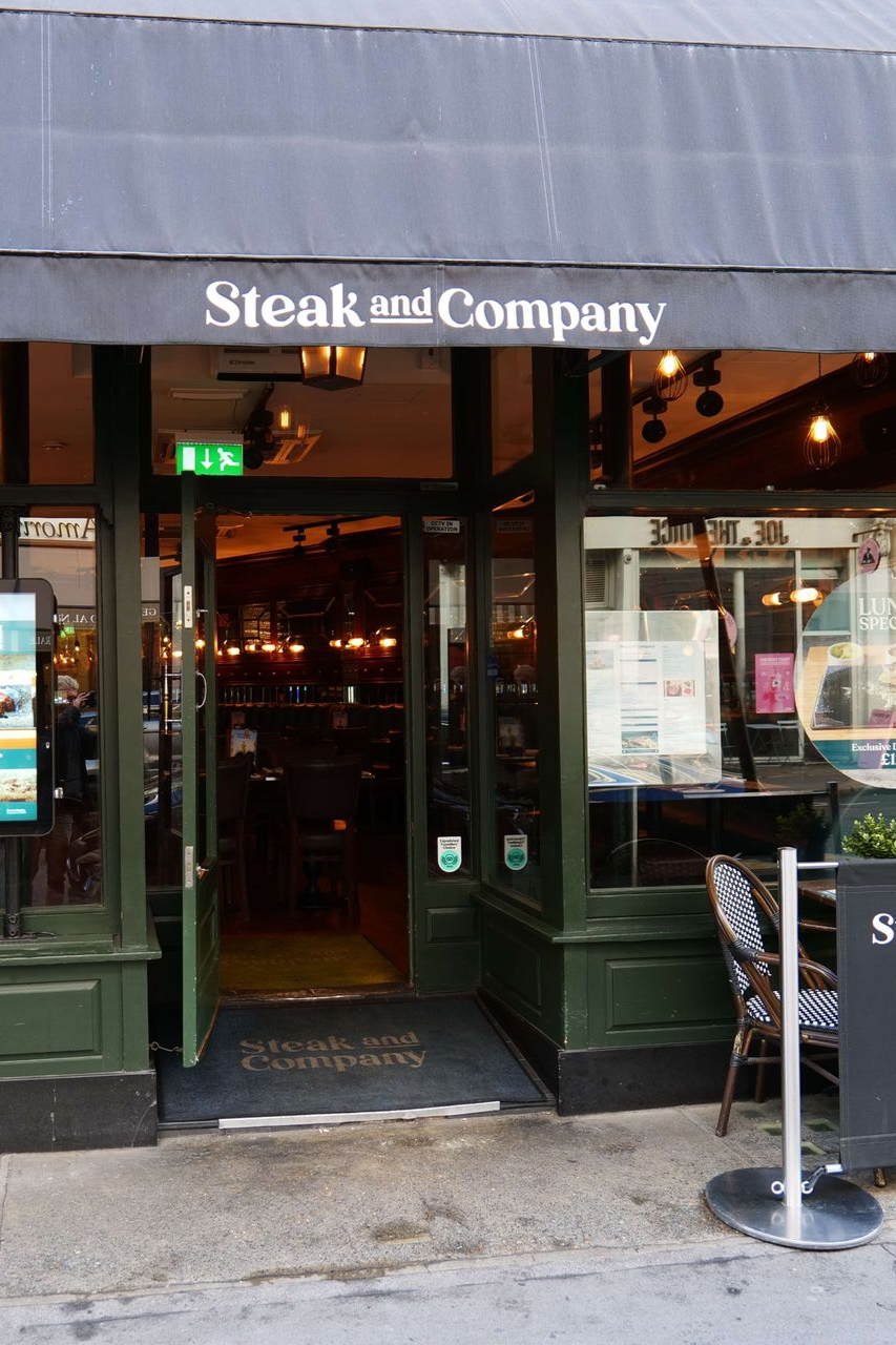 Steak and Company restaurant exterior with outdoor seating and a heating tower. People are seated at tables.