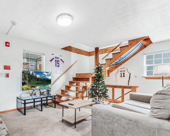 Living room with stairs, TV, and Christmas tree. Two sports jerseys hung on the wall.