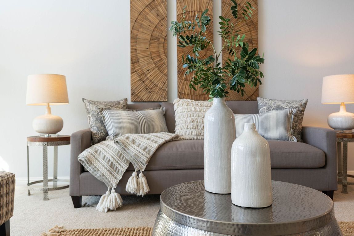 Living room with gray sofa, neutral decor, wood accent wall, white vases, and lamps.