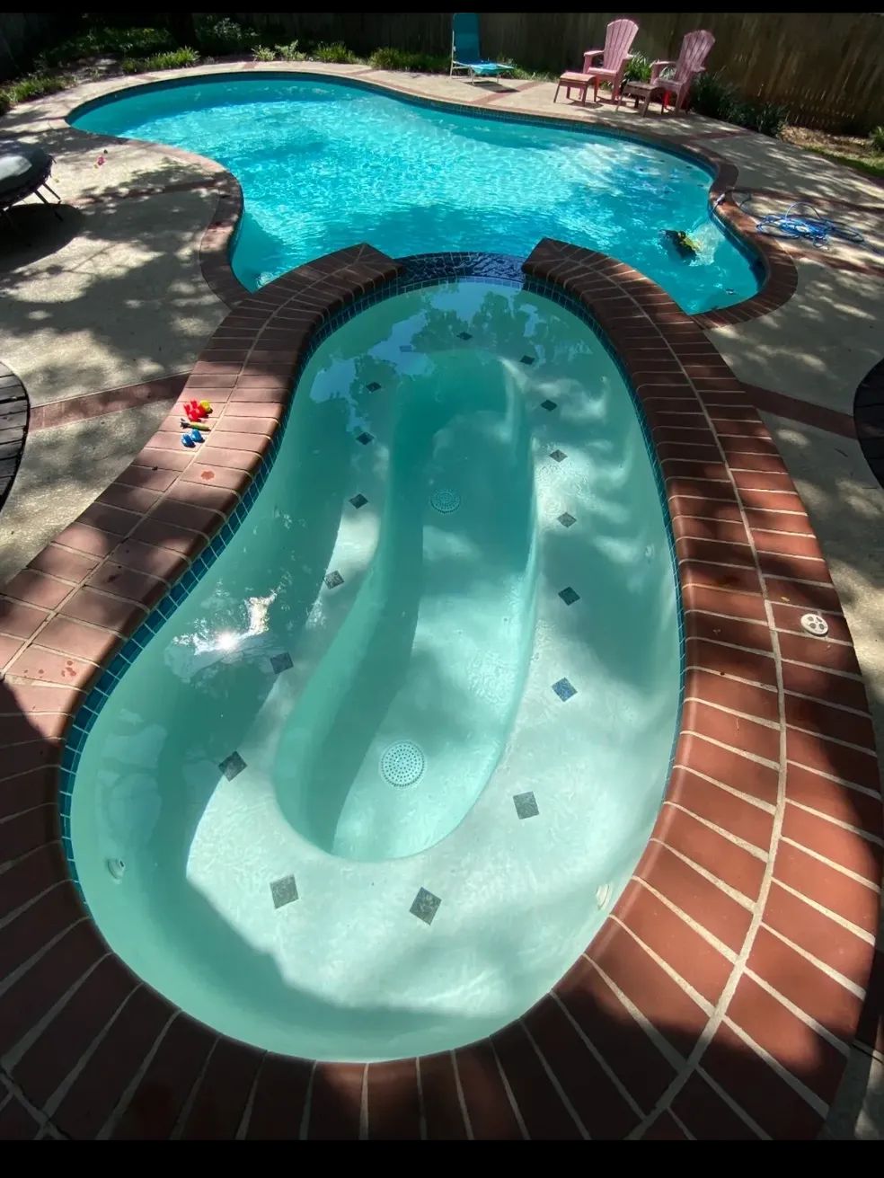 A backyard pool with a connecting jacuzzi. The pool is turquoise with red brick around the edges.