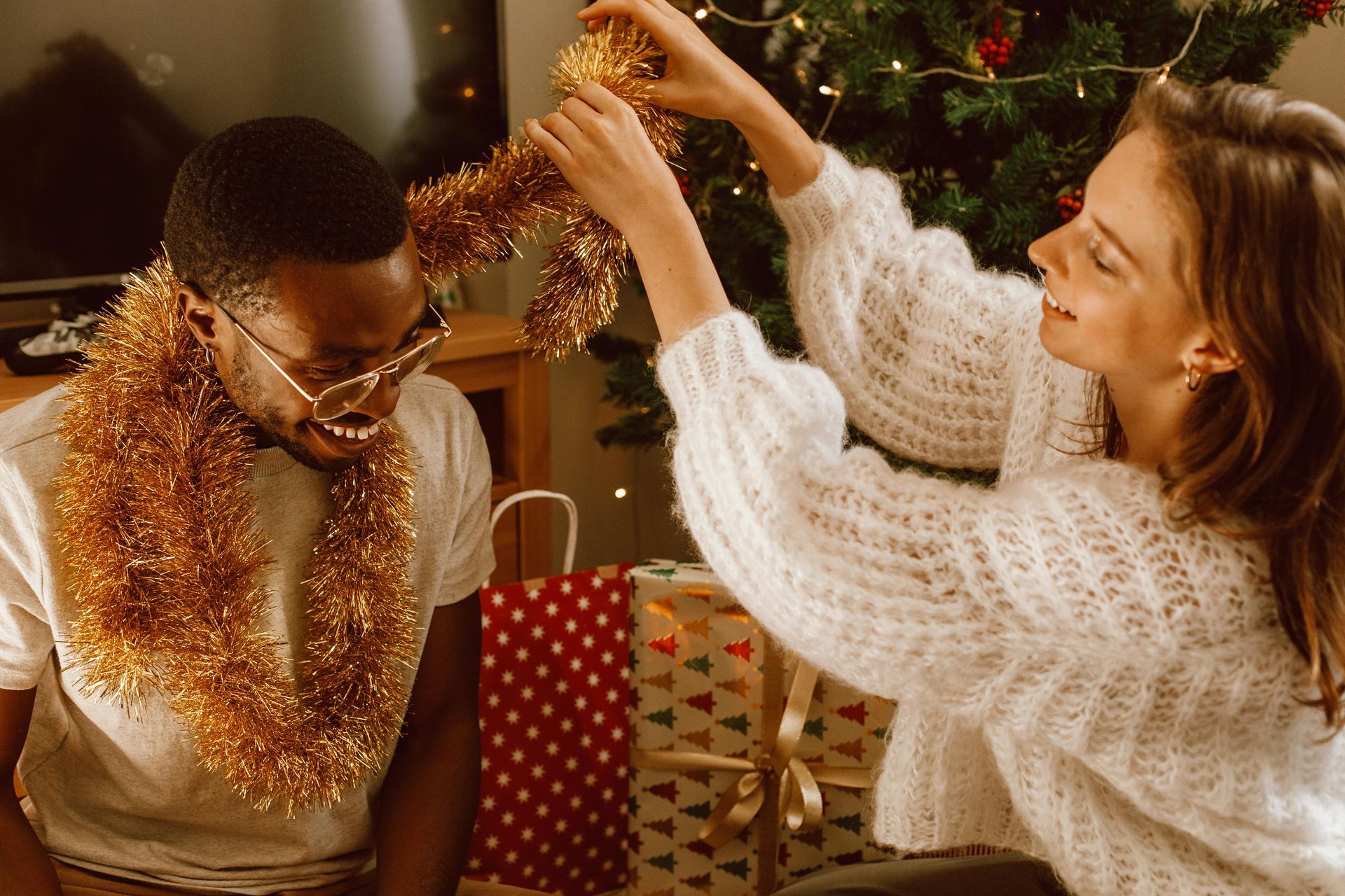 A man and a woman are decorating a christmas tree with tinsel.