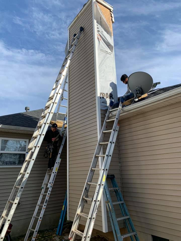 Two men are working on a chimney on the side of a house.