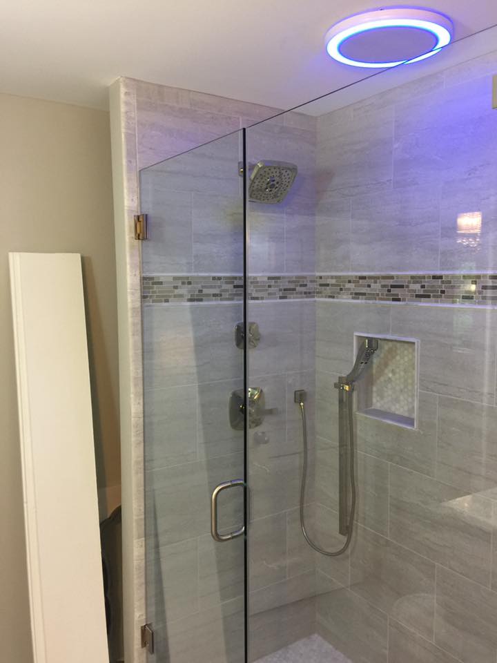 A shower with a glass door and a blue light on the ceiling.