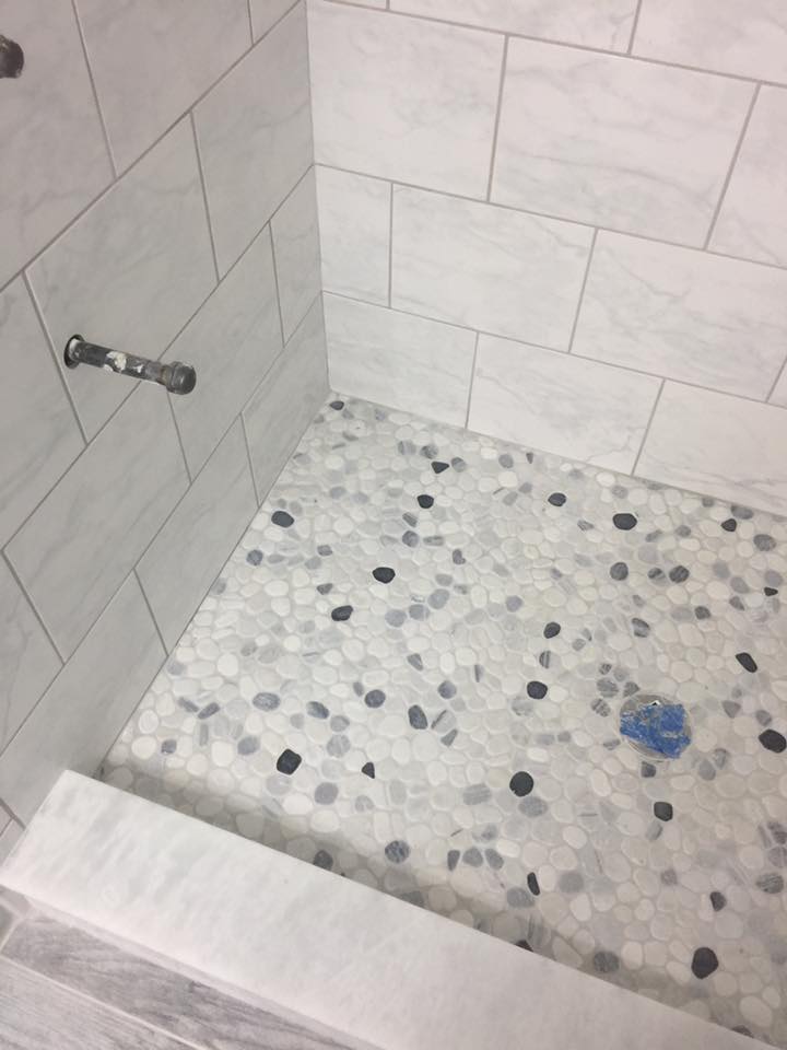 A shower stall with white tiles and a blue drain.