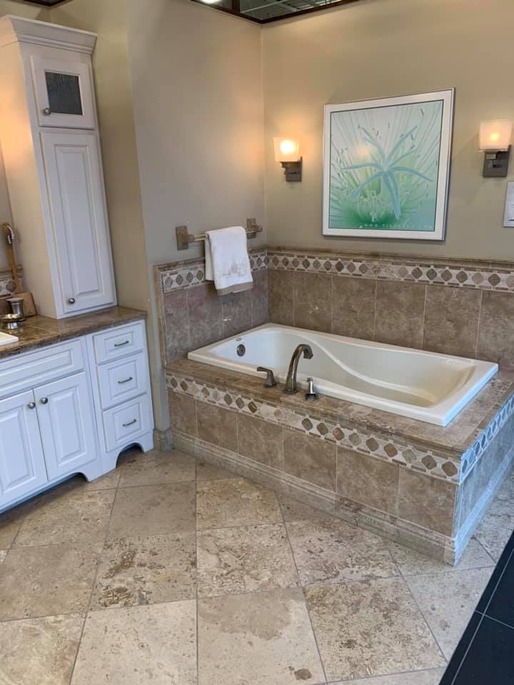 A bathroom with a tub , sink , cabinets and a picture on the wall.