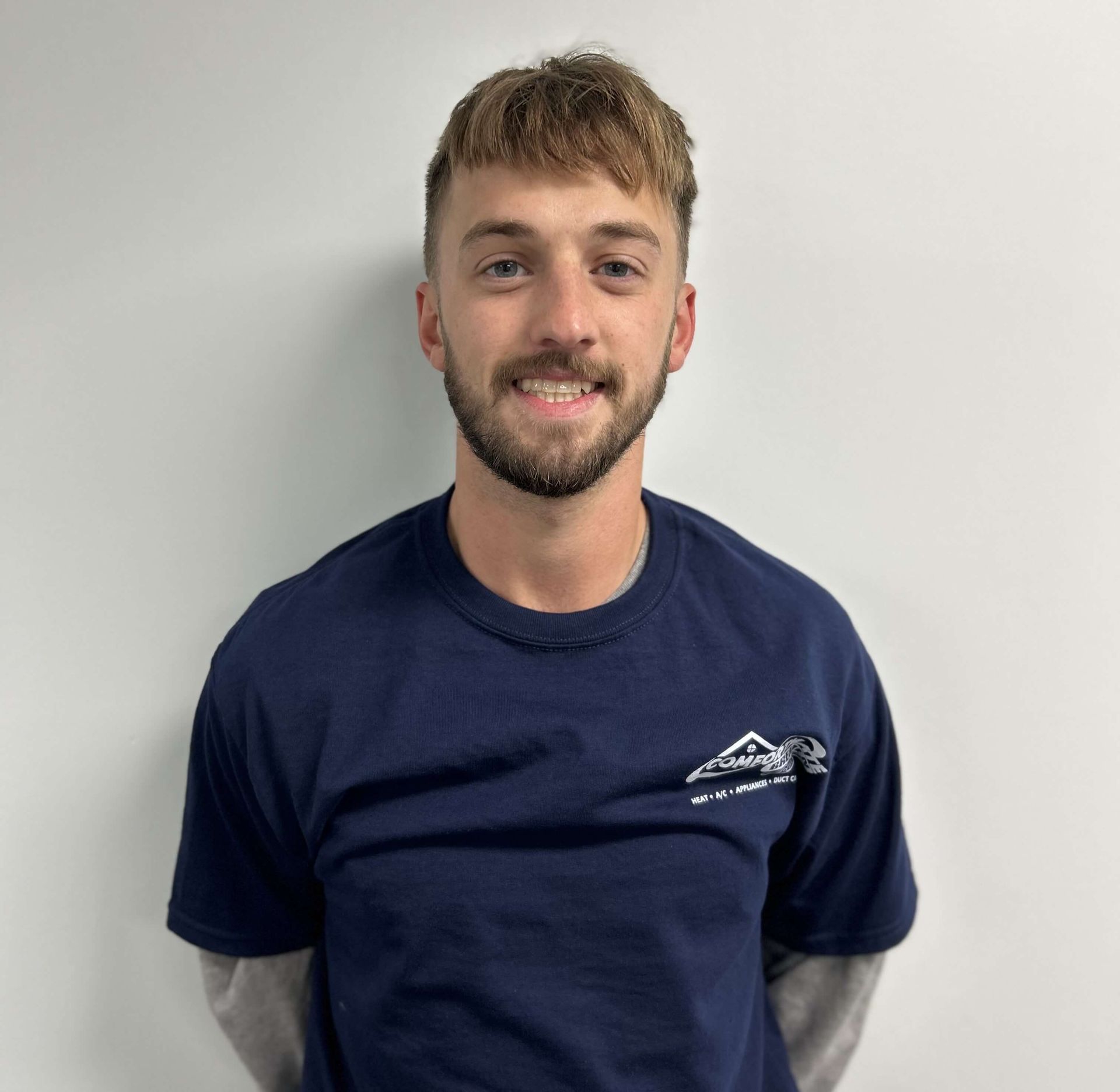 A young man with a beard is wearing a blue shirt and smiling.