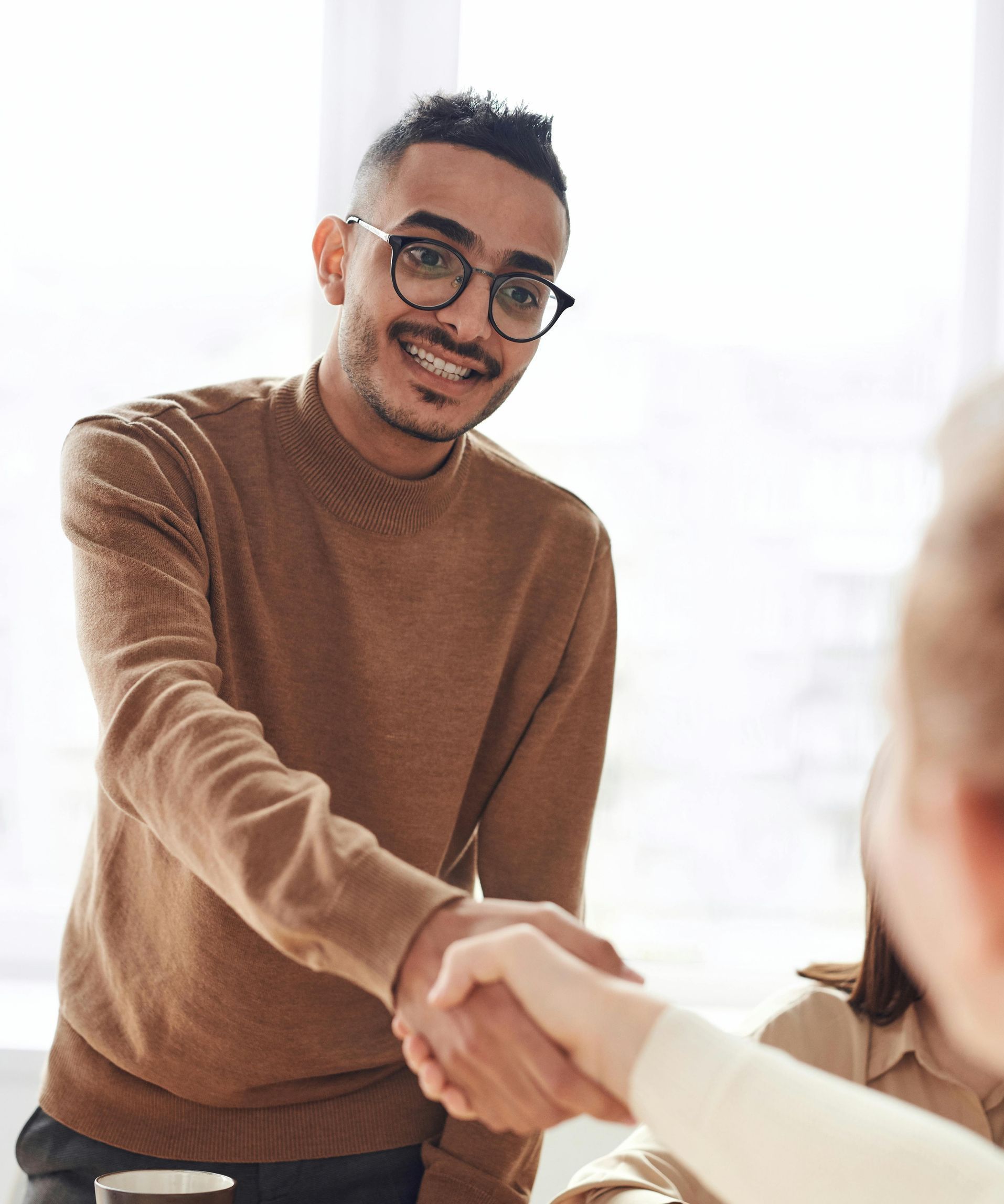 A man in a brown sweater is shaking hands with a woman.