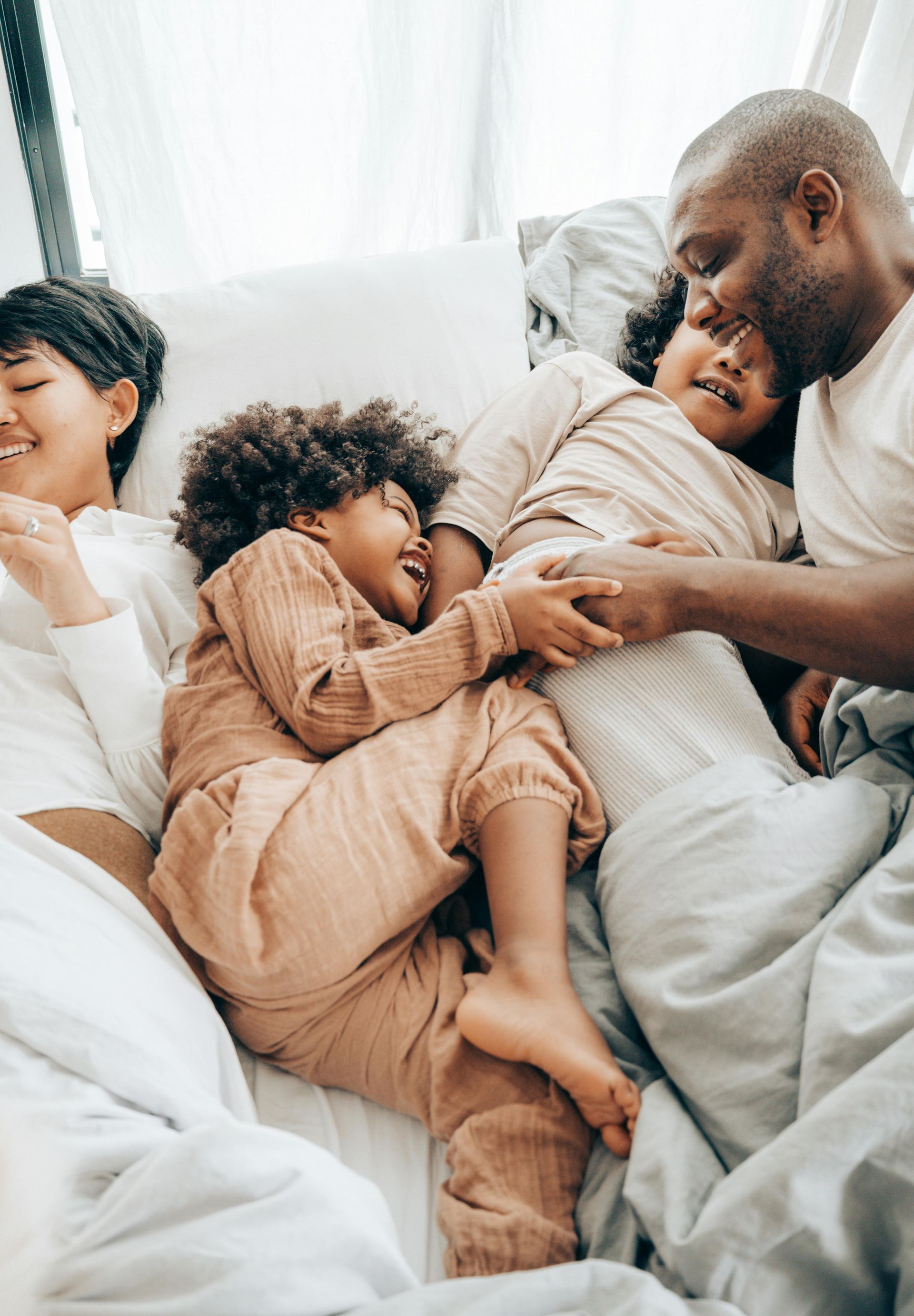 A family is laying in bed together and playing with each other.