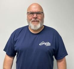A bald man with a beard and glasses is wearing a blue t-shirt.