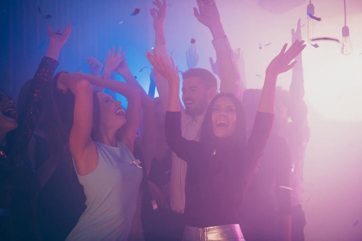 A group of people are dancing in a club with their hands in the air.