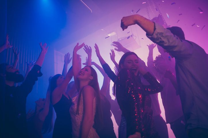 A group of people are dancing in a club with their hands in the air.