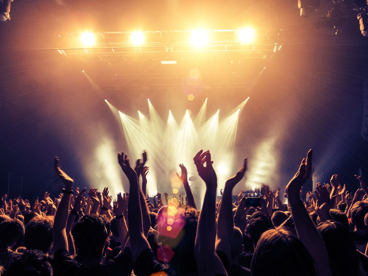 A crowd of people at a concert with their hands in the air